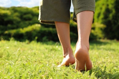 Photo of Woman walking barefoot on green grass outdoors, closeup. Space for text