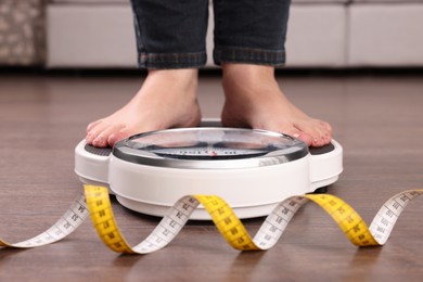 Woman using scales on floor near measuring tape, closeup. Overweight problem