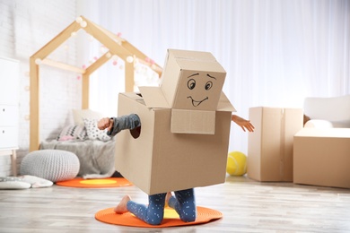 Photo of Cute little child wearing cardboard costume in bedroom