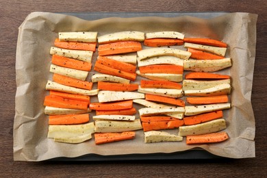 Photo of Baking tray with parchment, parsnips and carrots on wooden table, top view