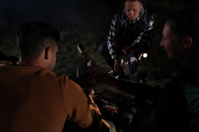 Group of friends roasting marshmallows on bonfire at camping site in evening