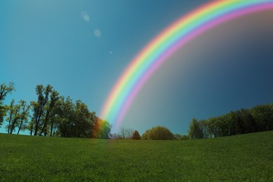 Image of Picturesque view of green meadow and beautiful rainbow in blue sky on sunny day