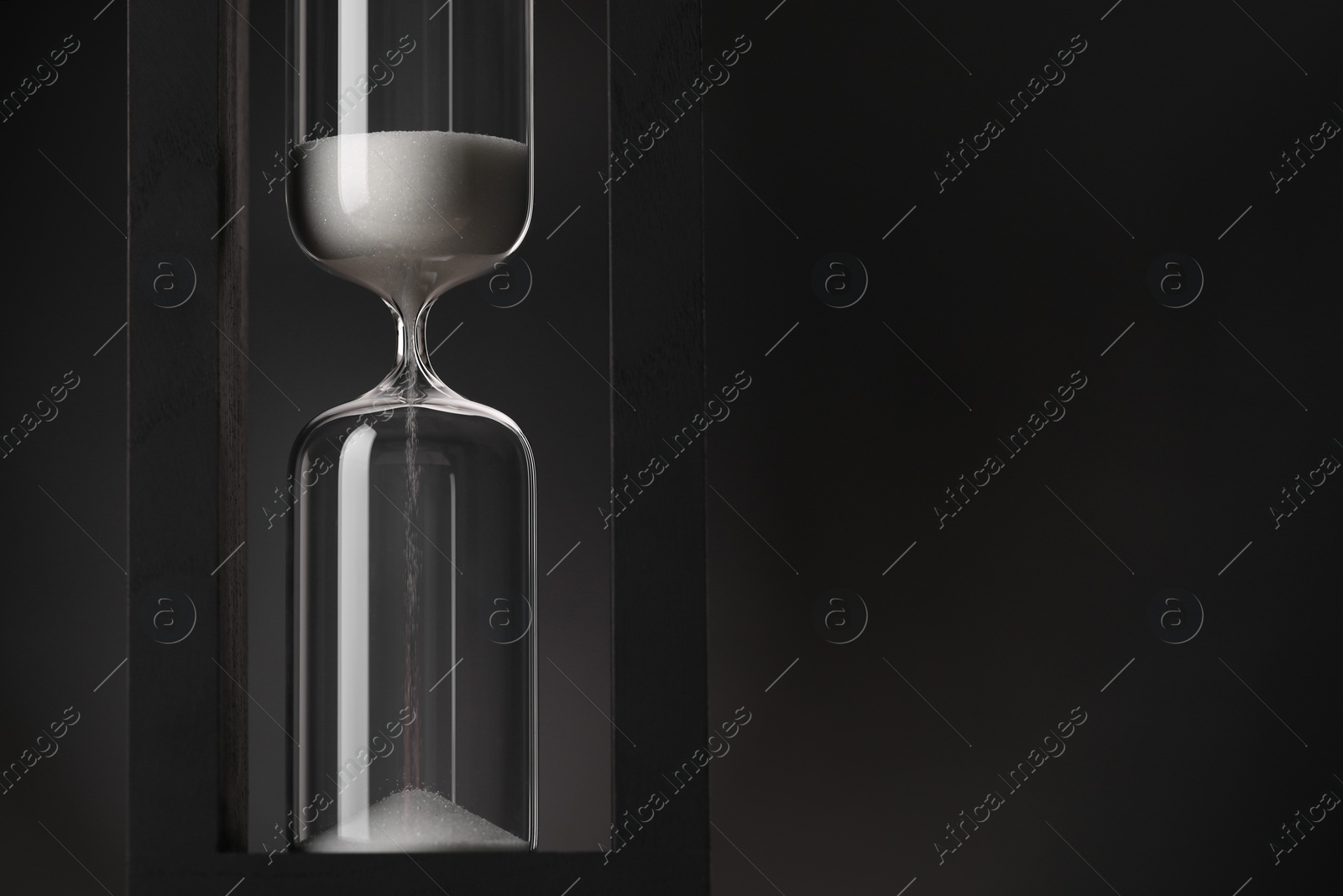 Photo of Hourglass with flowing sand on black background. Space for text