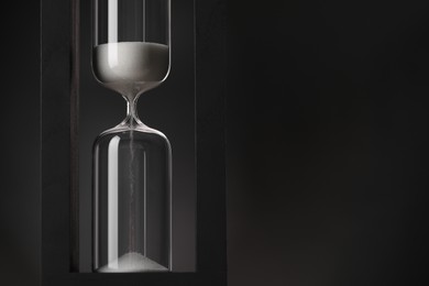 Photo of Hourglass with flowing sand on black background. Space for text