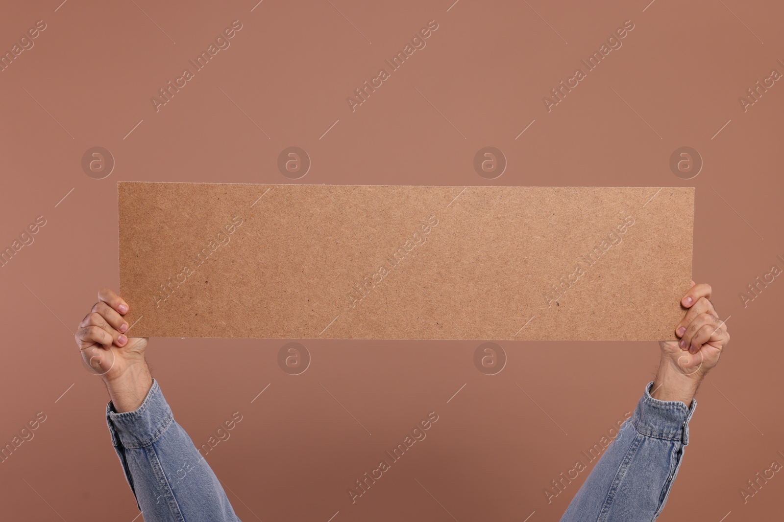 Photo of Man holding blank cardboard banner on brown background, closeup. Space for text