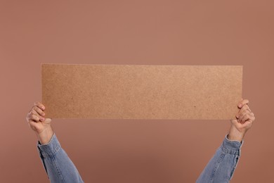 Man holding blank cardboard banner on brown background, closeup. Space for text