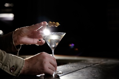 Photo of Barman adding olives to martini cocktail on counter, closeup. Space for text