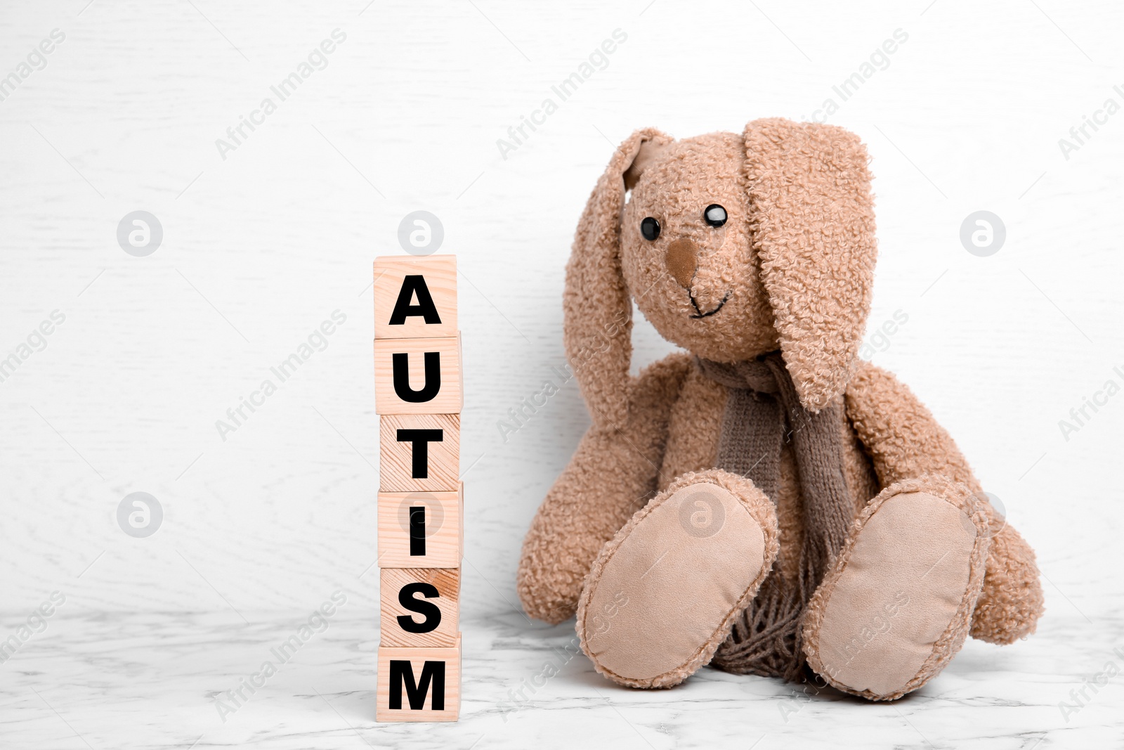 Photo of Toy bunny and wooden cubes with word AUTISM on table against light background