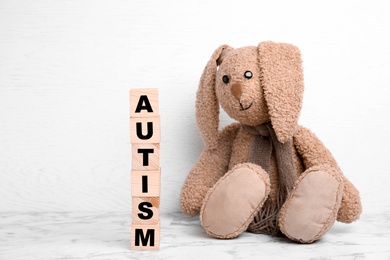 Photo of Toy bunny and wooden cubes with word AUTISM on table against light background