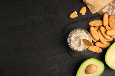 Photo of Delicious crackers, avocado and humus on black table, flat lay. Space for text