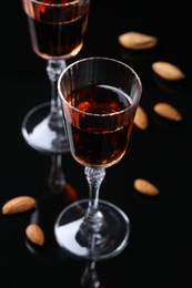 Photo of Liqueur glass with tasty amaretto and almonds on black table, closeup