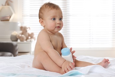 Adorable little baby with bottle of dusting powder on bed at home