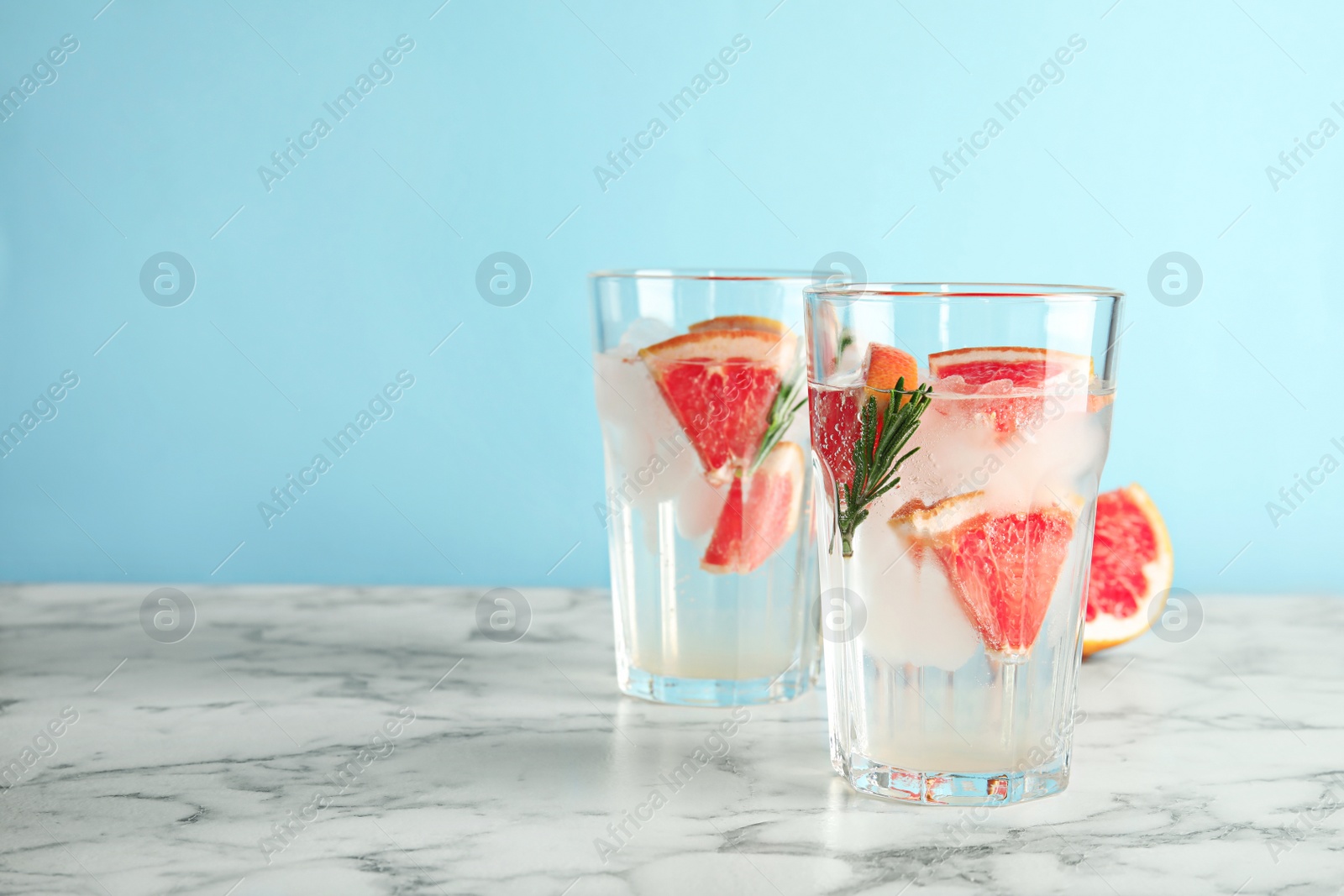 Photo of Glasses of infused water with grapefruit slices on table against color background. Space for text