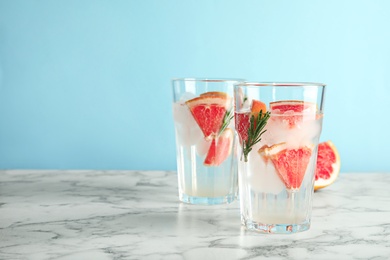 Glasses of infused water with grapefruit slices on table against color background. Space for text