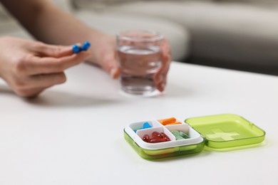 Photo of Woman with pills, organizer and glass of water at white table, selective focus