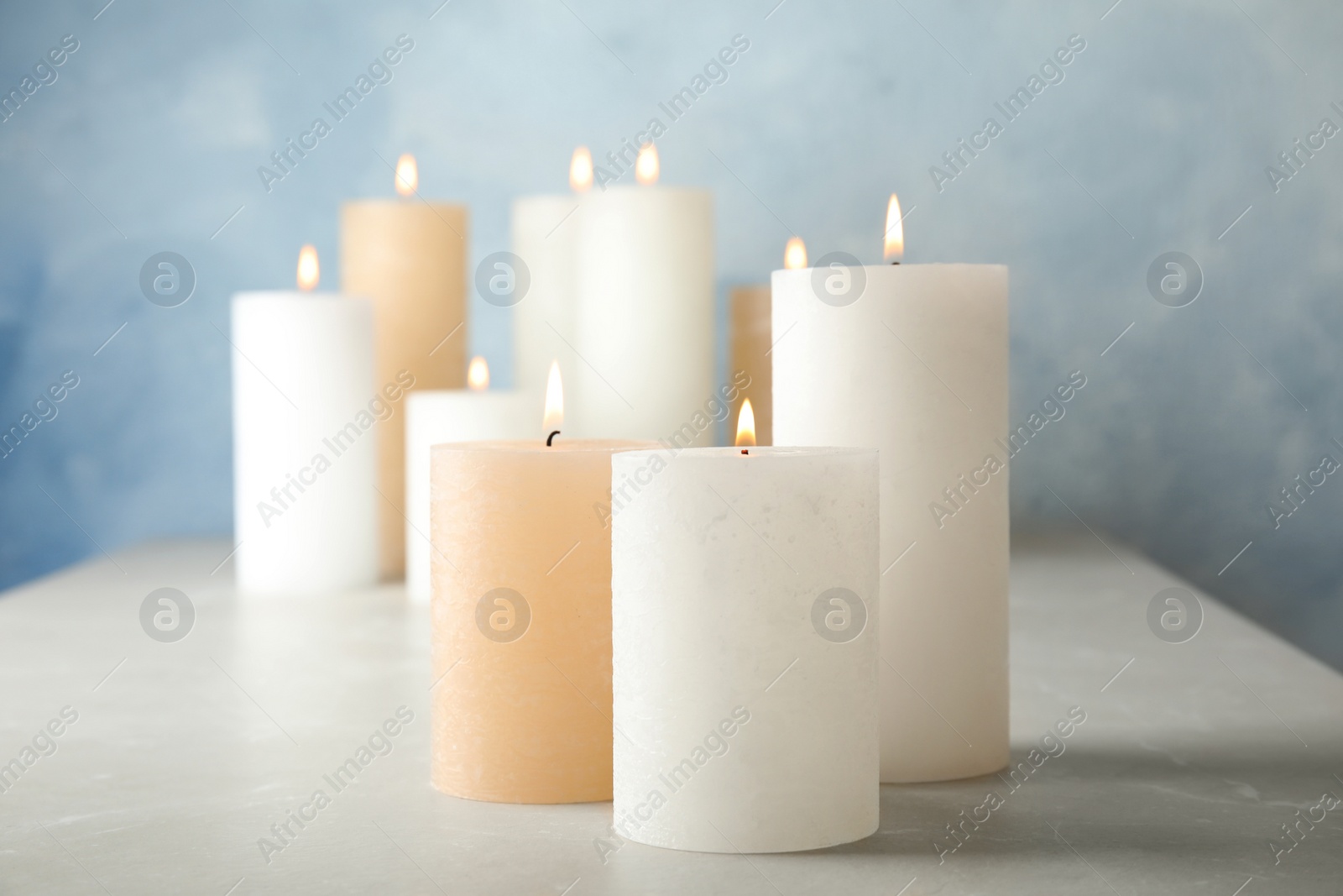 Photo of Burning candles on table against color background