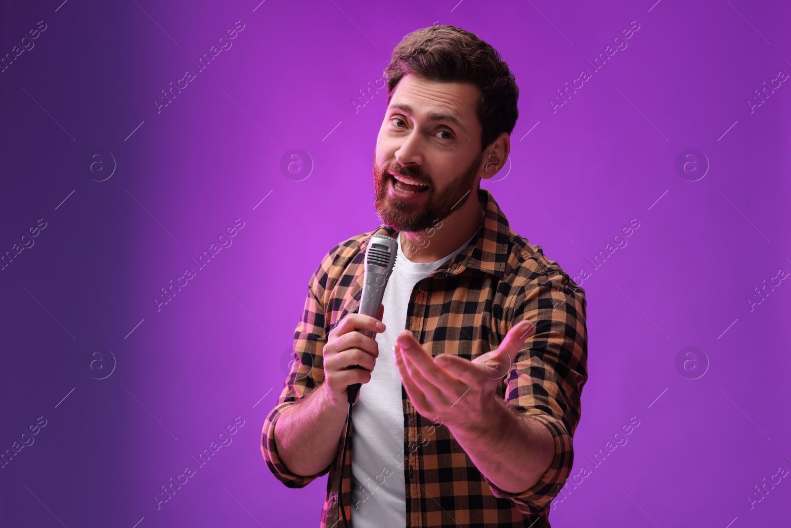 Photo of Handsome man with microphone singing on purple background. Space for text