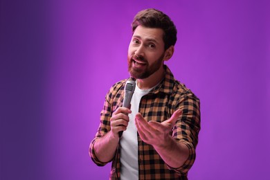 Handsome man with microphone singing on purple background. Space for text