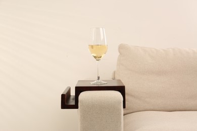 Photo of Glass of white wine on sofa with wooden armrest table indoors. Interior element