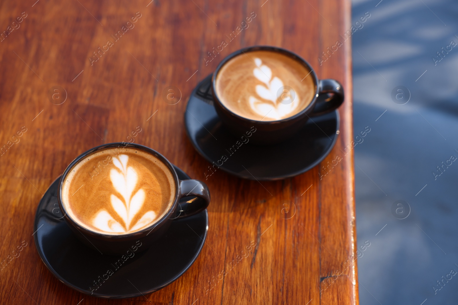 Photo of Cups of aromatic coffee with foam on wooden table in outdoor cafe. Space for text