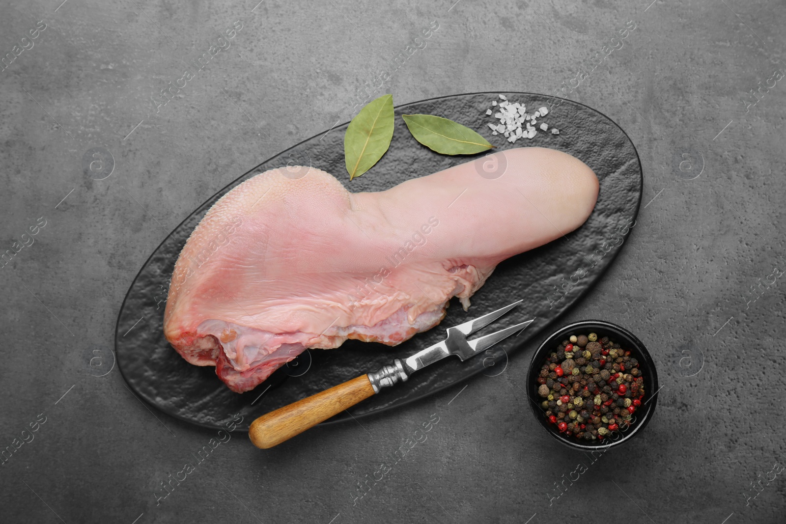 Photo of Serving board with raw beef tongue, peppercorns and bay leaves on grey table, flat lay