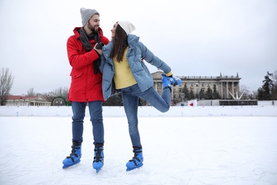 Happy couple skating along ice rink outdoors. Space for text