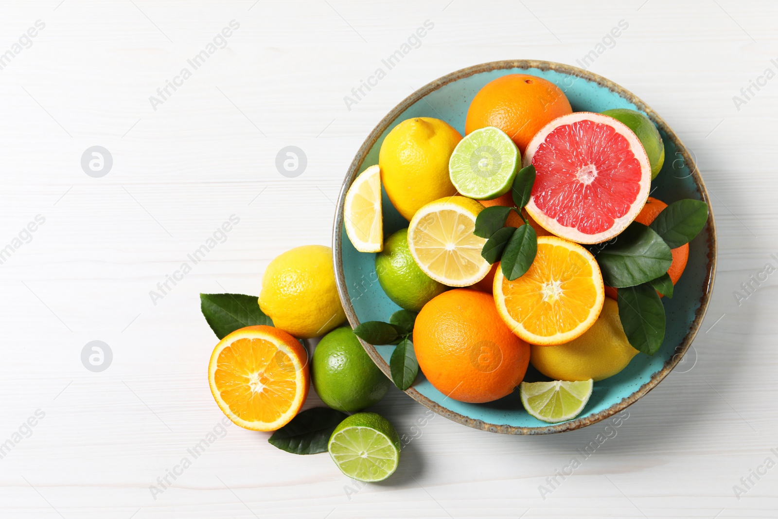 Photo of Different cut and whole citrus fruits on white wooden table, top view. Space for text