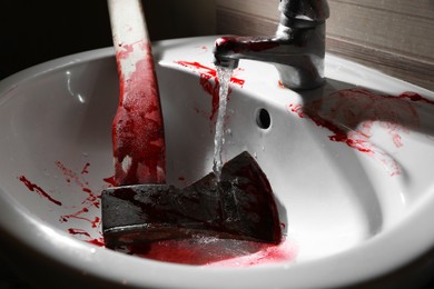 Axe with blood under tap water in sink, closeup