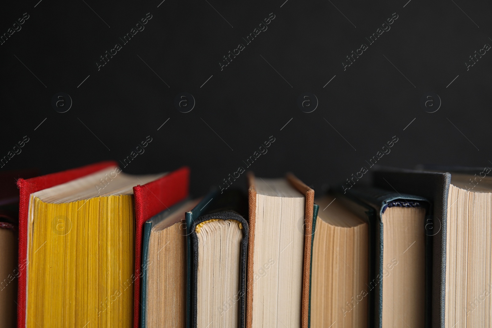 Photo of Stack of hardcover books on black background, closeup. Space for text