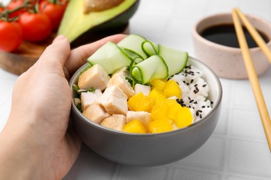 Photo of Woman holding delicious poke bowl with meat, rice and vegetables at white table, closeup