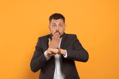 Emotional man checking time on orange background. Being late concept