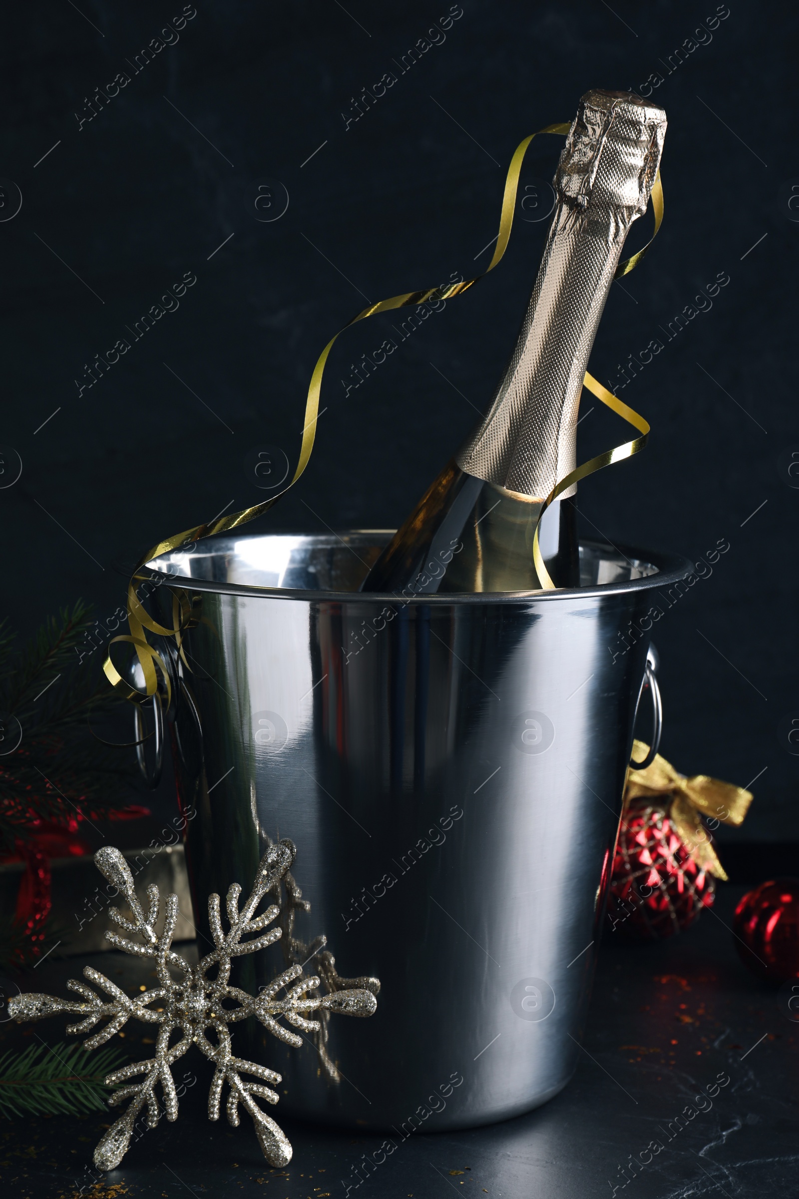 Photo of Happy New Year! Bottle of sparkling wine in bucket and festive decor on black background