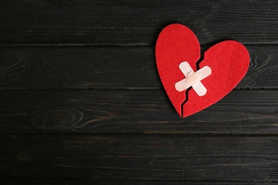 Halves of cut felt heart joined with adhesive plasters on dark wooden background, top view. Space for text