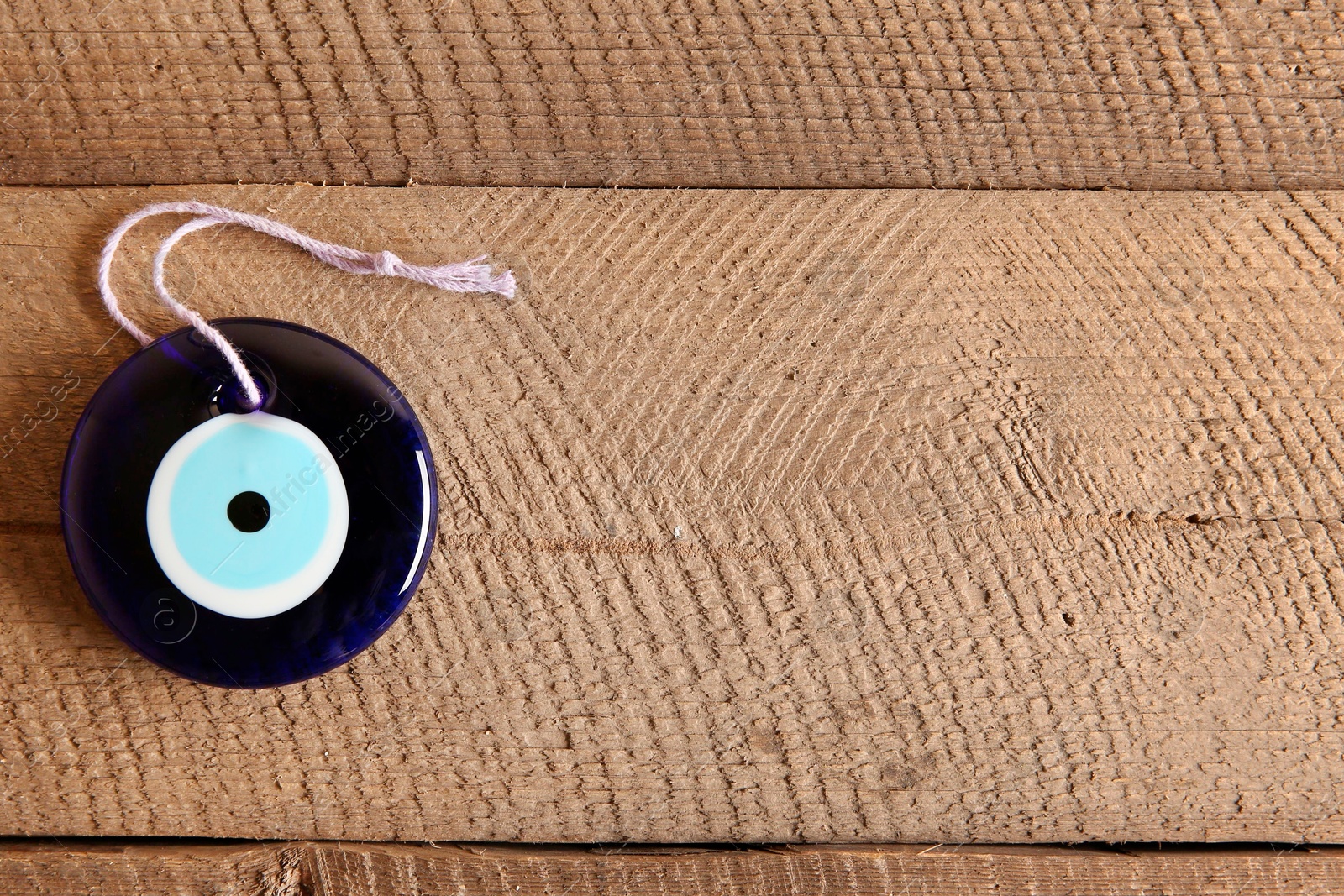 Photo of Evil eye amulet on wooden table, top view. Space for text