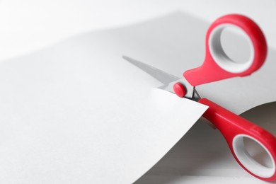 Red scissors cutting paper on white wooden background, closeup