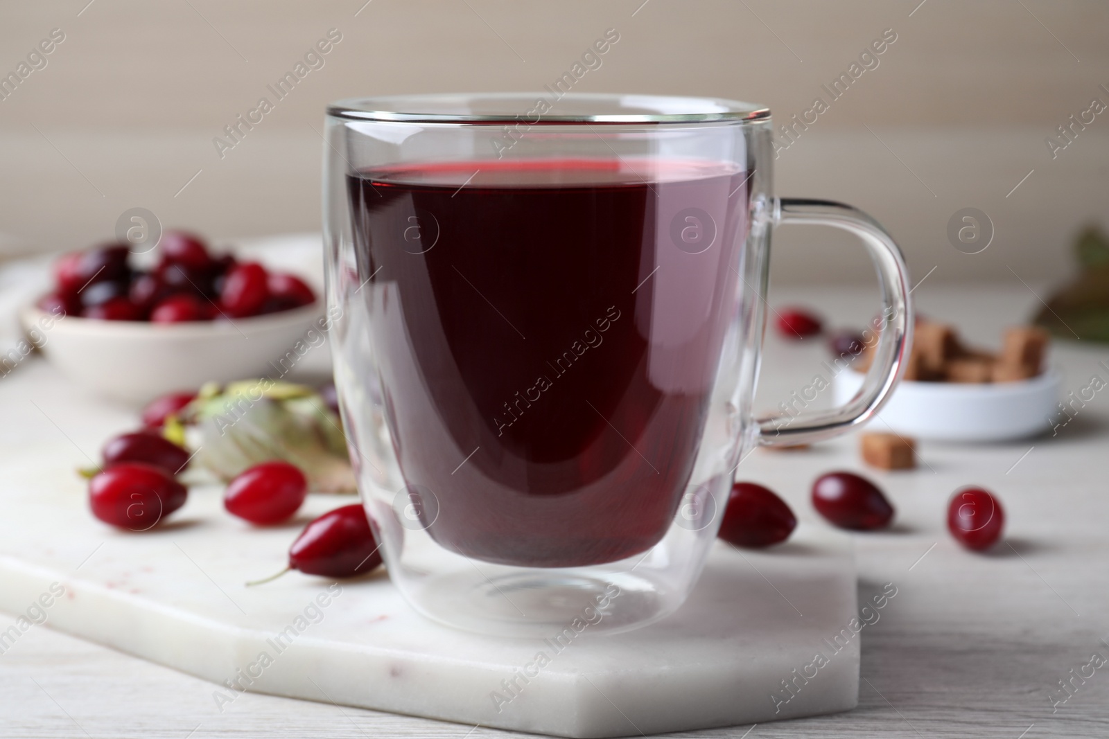 Photo of Glass cup of fresh dogwood tea and berries on white wooden table