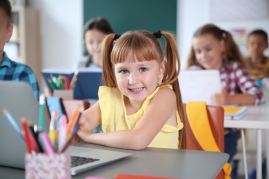 Cute little child with laptop sitting at desk in classroom. Elementary school