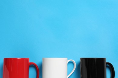 Photo of Colorful ceramic mugs on light blue background, flat lay. Space for text