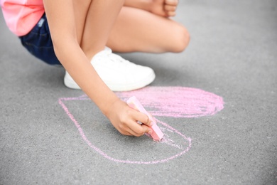 Little child drawing heart with chalk on asphalt, closeup