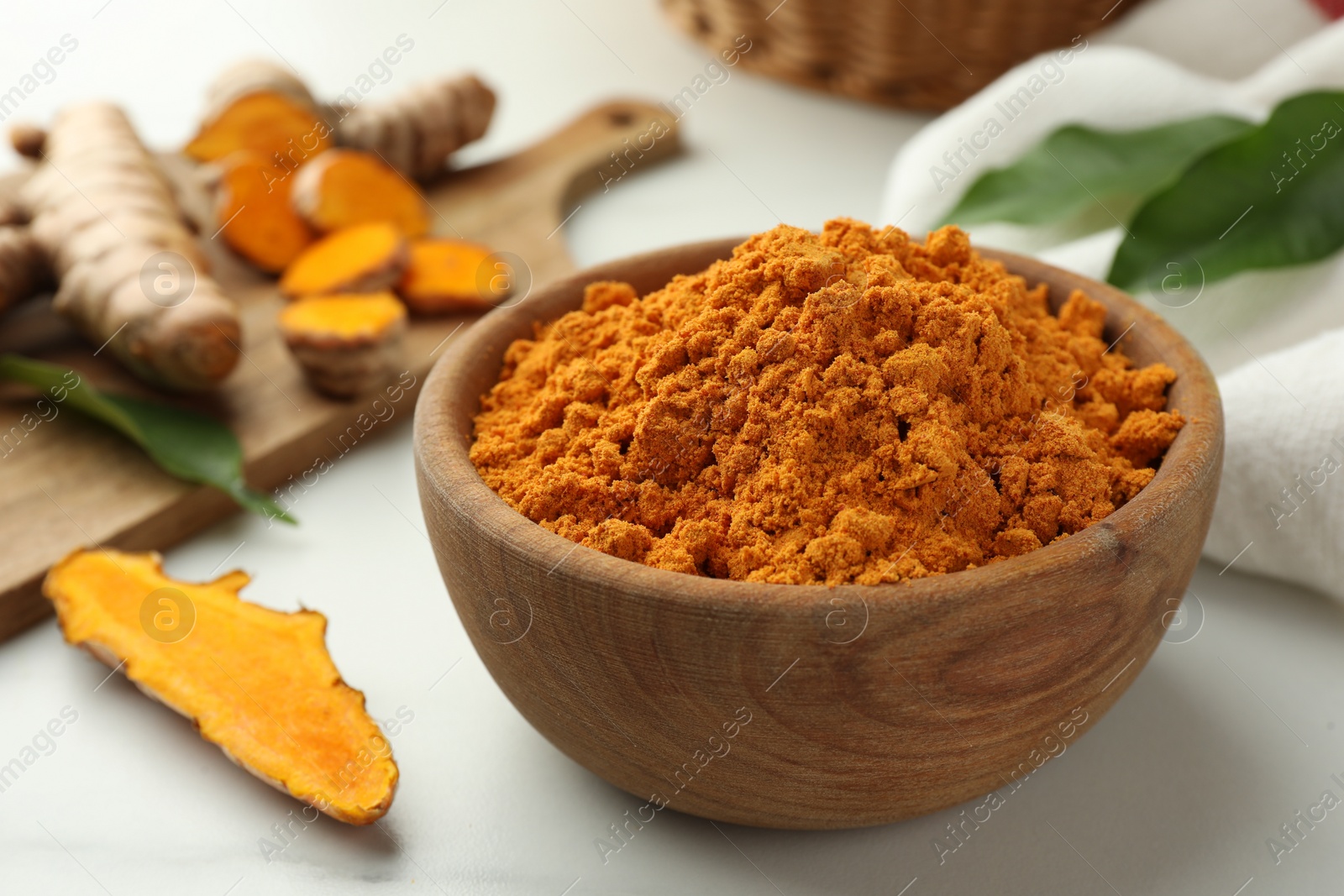 Photo of Aromatic turmeric powder and raw roots on white table, closeup