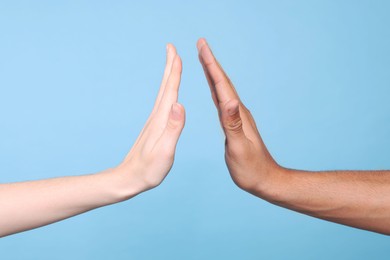 Photo of International relationships. People giving high five on light blue background, closeup