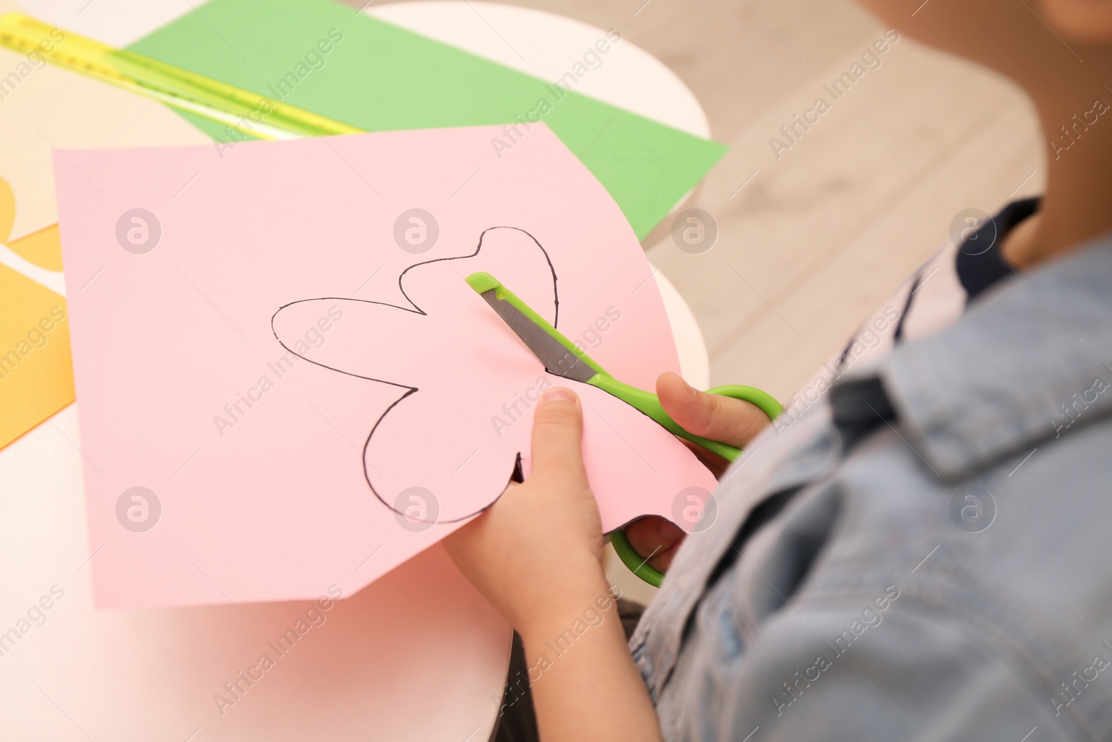 Photo of Little boy cutting color paper with scissors at table indoors, closeup