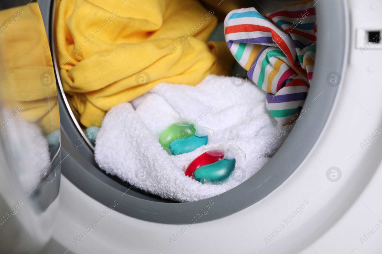 Photo of Laundry detergent capsules and clothes in washing machine drum, closeup view