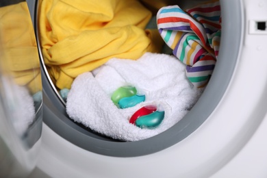 Laundry detergent capsules and clothes in washing machine drum, closeup view