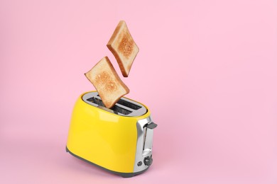 Photo of Bread slices popping up from modern toaster on pink background. Space for text