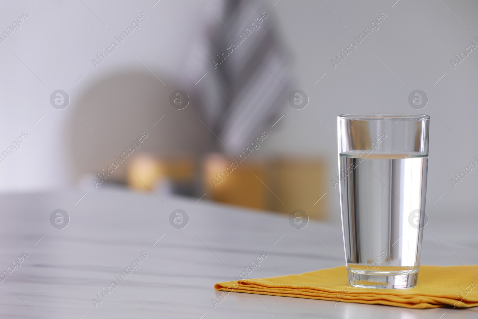 Photo of Glass of water and napkin on white table against blurred background. Space for text