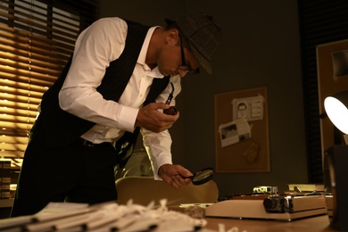 Photo of Old fashioned detective with smoking pipe and magnifying glass working in office
