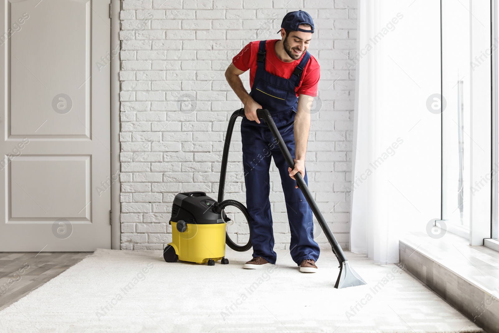 Photo of Male worker cleaning carpet with vacuum indoors