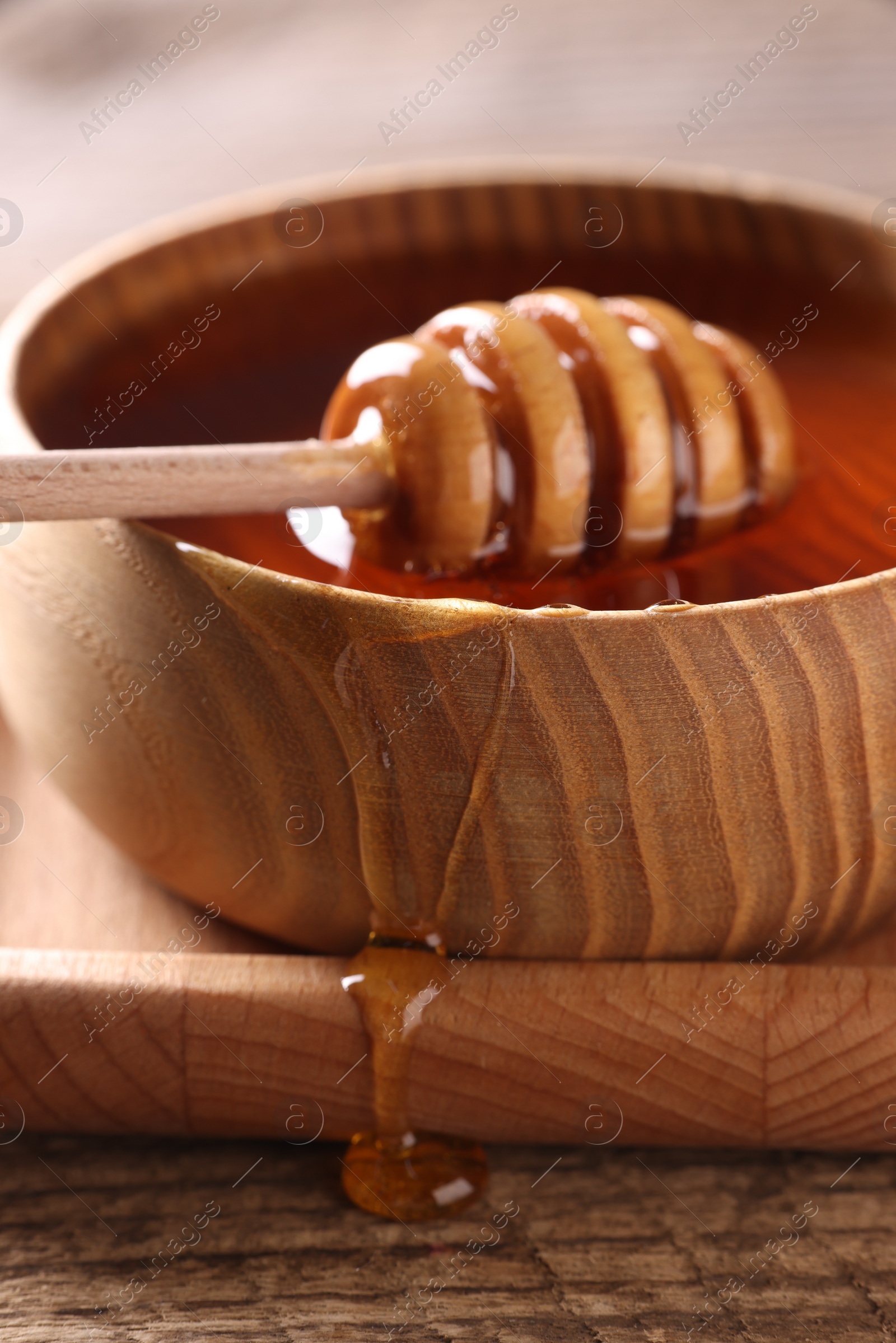 Photo of Delicious honey in bowl and dipper on wooden table, closeup