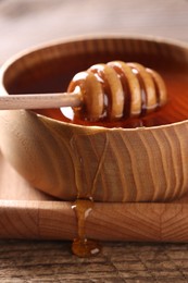 Photo of Delicious honey in bowl and dipper on wooden table, closeup